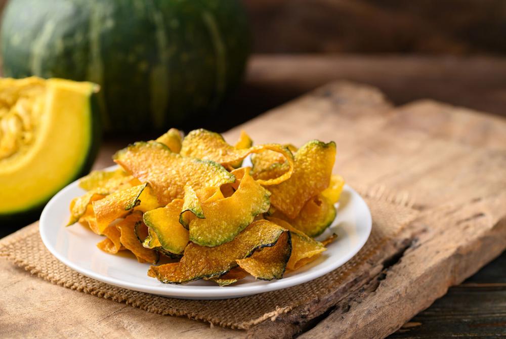 Chips de citrouille maison pour Halloween dans une assiette sur table en bois, prêtes à croquer