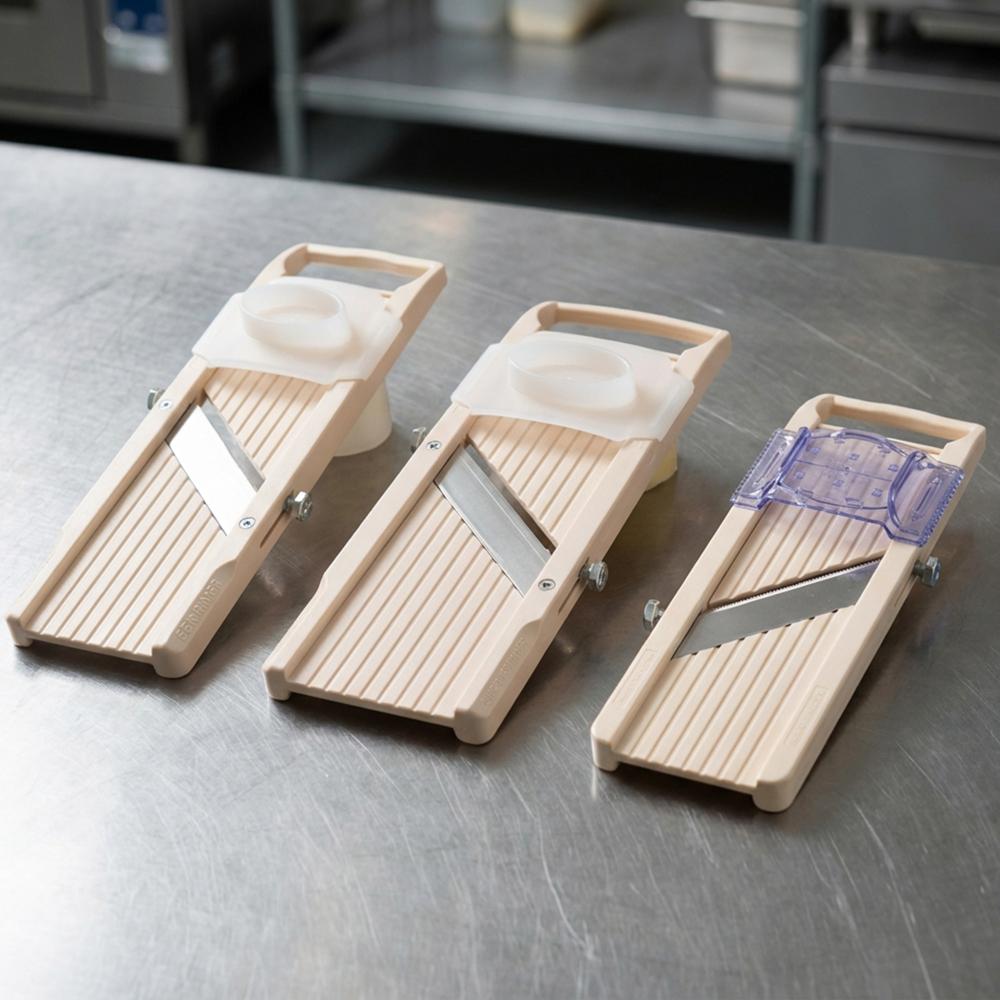 Découvrez les différents modèles de mandolines japonaises Benriner de la gamme standard Gamme de trois mandolines de cuisine Benriner de tailles différentes avec leurs poussoirs de protection respectifs posées sur un plan de travail en inox.
