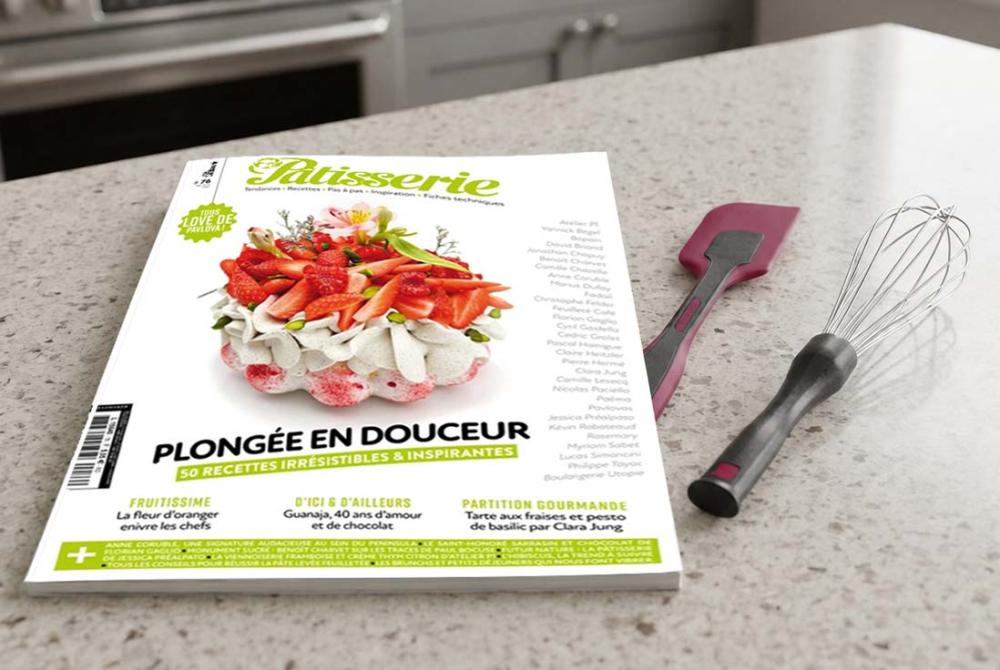 Magazine Fou de P&acirc;tisserie pos&eacute; sur un plan de travail en pierre avec une maryse et un fouet de la marque Gobel.