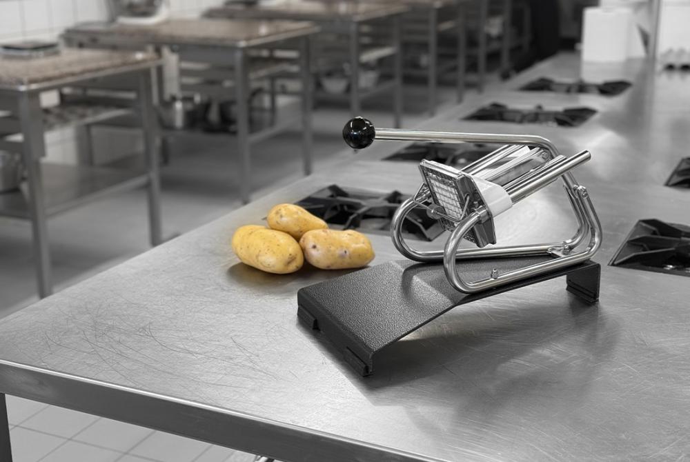 image d'un coupe frites de la marque Louis Tellier. Coupe frites posé sur un plan de travail en inox d'une cuisine professionnelle avec des pommes de terre entières posées à côté