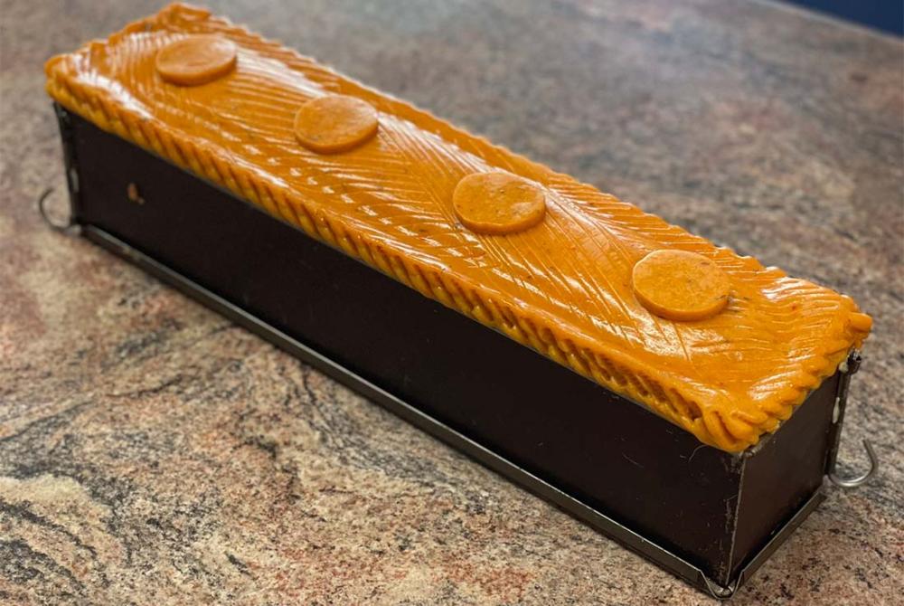 Image d'un pâté en croûte doré dans son moule Gobel, posé sur un plan de travail.