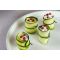 Quatre amuse-bouches en forme de rouleaux, composés de fines tranches de courgette garnies de crème blanche et surmontées de baies roses, sur une assiette