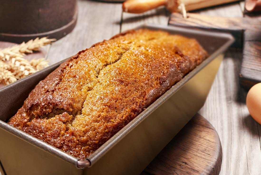 Pain aux epices doré dans un moule à pain Gobel posé sur une surface en bois, entouré d'œufs, de tiges de blé et d'un rouleau à pâtisserie, qui dégage une impression de chaleur et de convivialité.